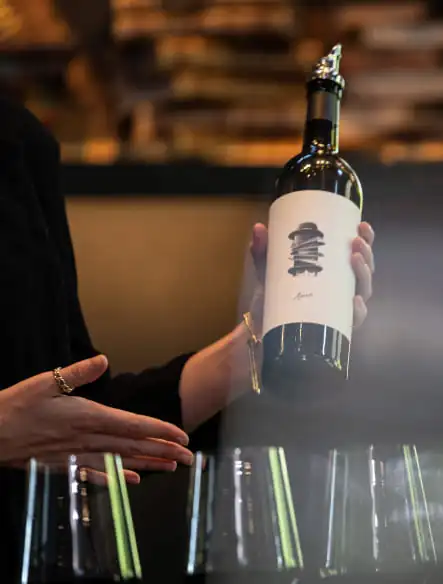 A woman holding a bottle of wine in front of glasses.