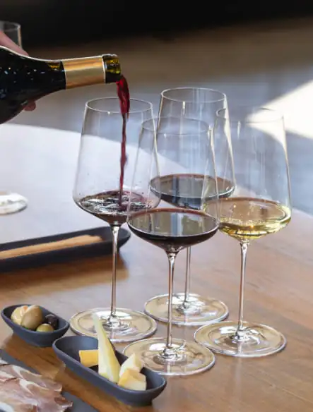 A person pouring wine into glasses on a table.