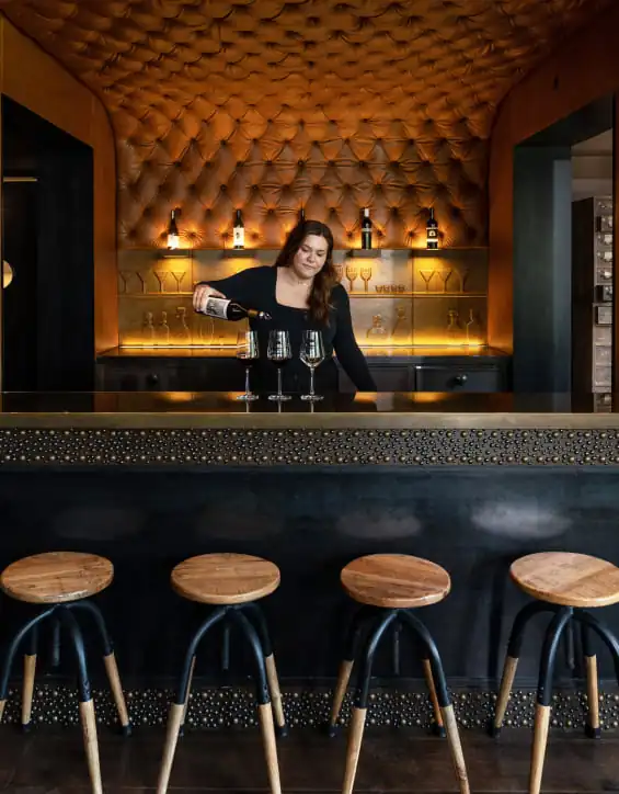 A woman is standing behind a bar with stools.