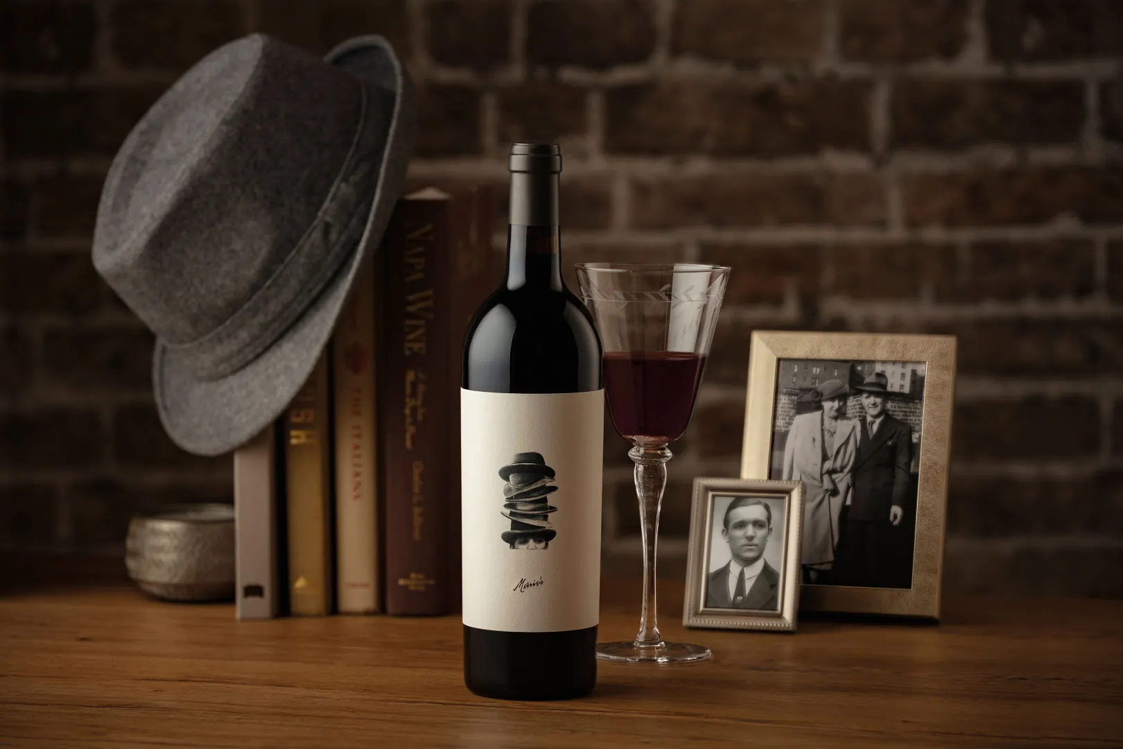 A bottle of red wine on a table next to a hat.