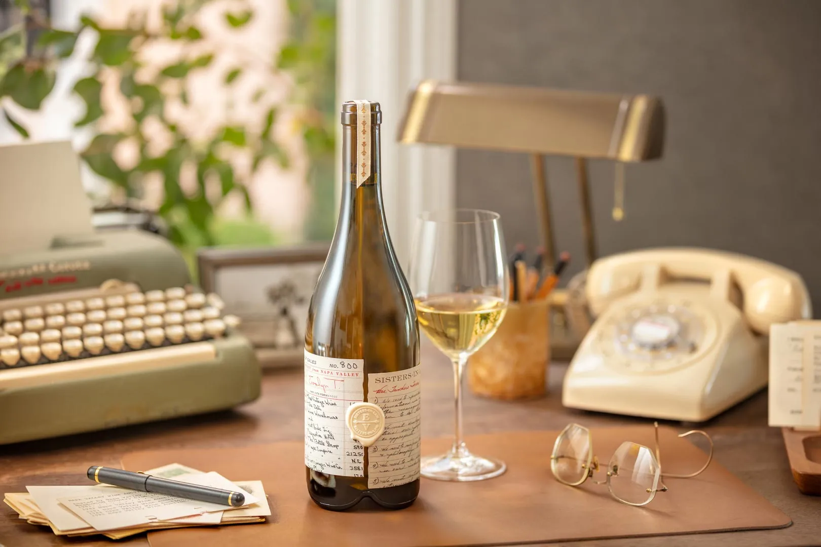 A bottle of wine sits on a desk next to a typewriter.