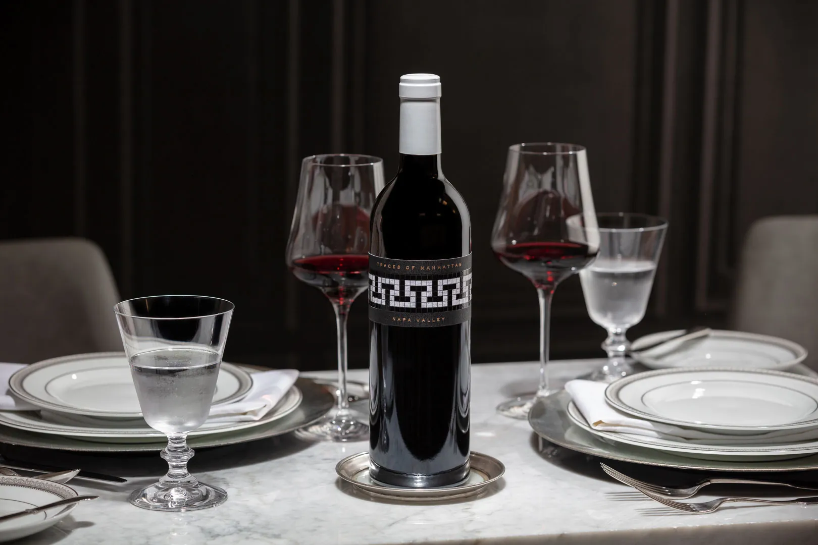 A bottle of wine on a table with glasses and plates.