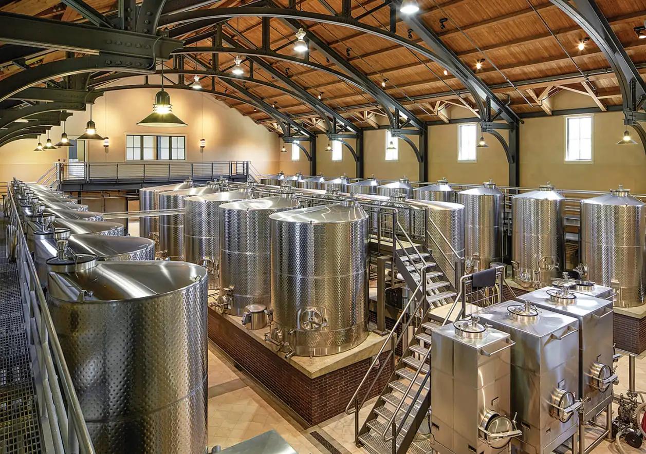 The inside of a large winery with many stainless steel tanks.